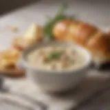 A bowl of traditional clam chowder with fresh herbs and a bread roll